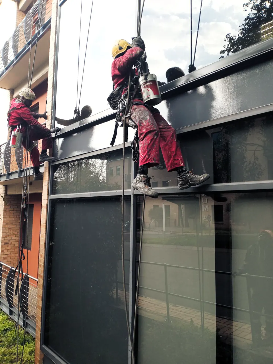 Two MP technicians on ropes repainting a dark steel fascia on an apartment block