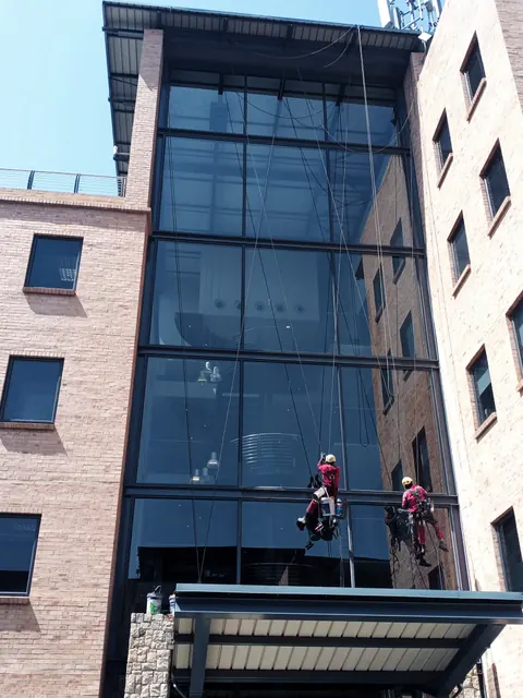 Two MP technicians working on a glass curtain wall above an entrance canopy