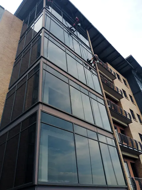 View up a glass corner tower with two MP technicians on ropes near the top