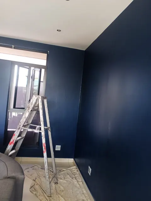 Room with a freshly painted navy wall and a stepladder on drop sheets
