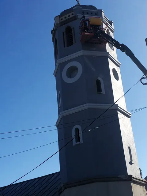 Technician in a cherry-picker basket working near the top of a church tower