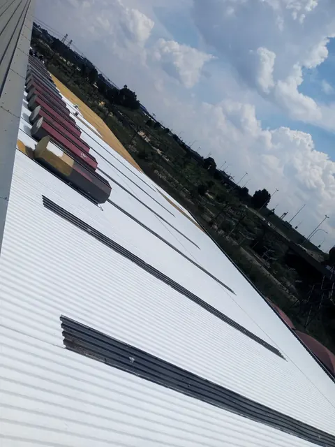 Coated white roof sheets running up to the roof ridge under a cloudy sky