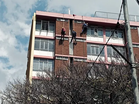MP technicians on ropes on a brick high-rise, seen through bare trees