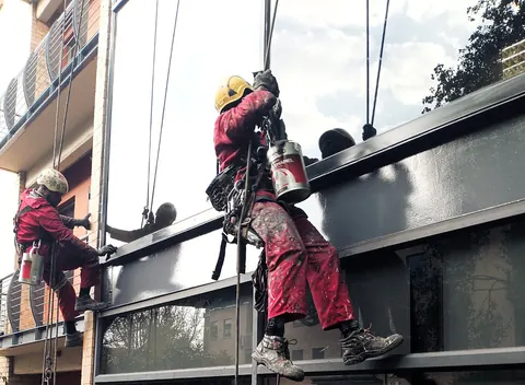 Two MP technicians on ropes repainting a dark steel fascia on an apartment block